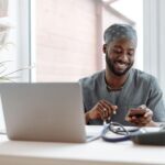 Smiling healthcare professional using phone in office with laptop and medical tools.